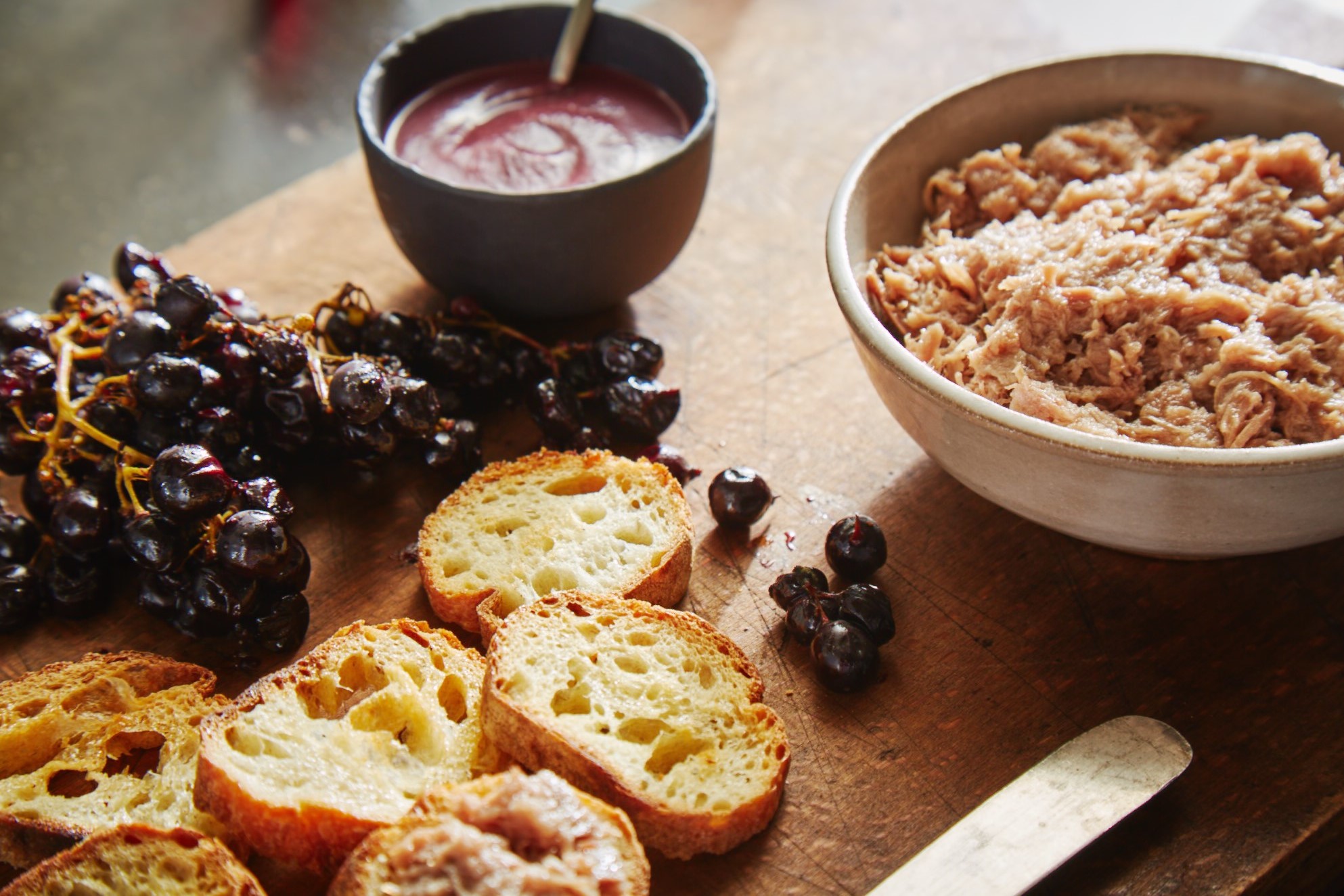 Grapes and bread on a cutting board with duck rillettes.